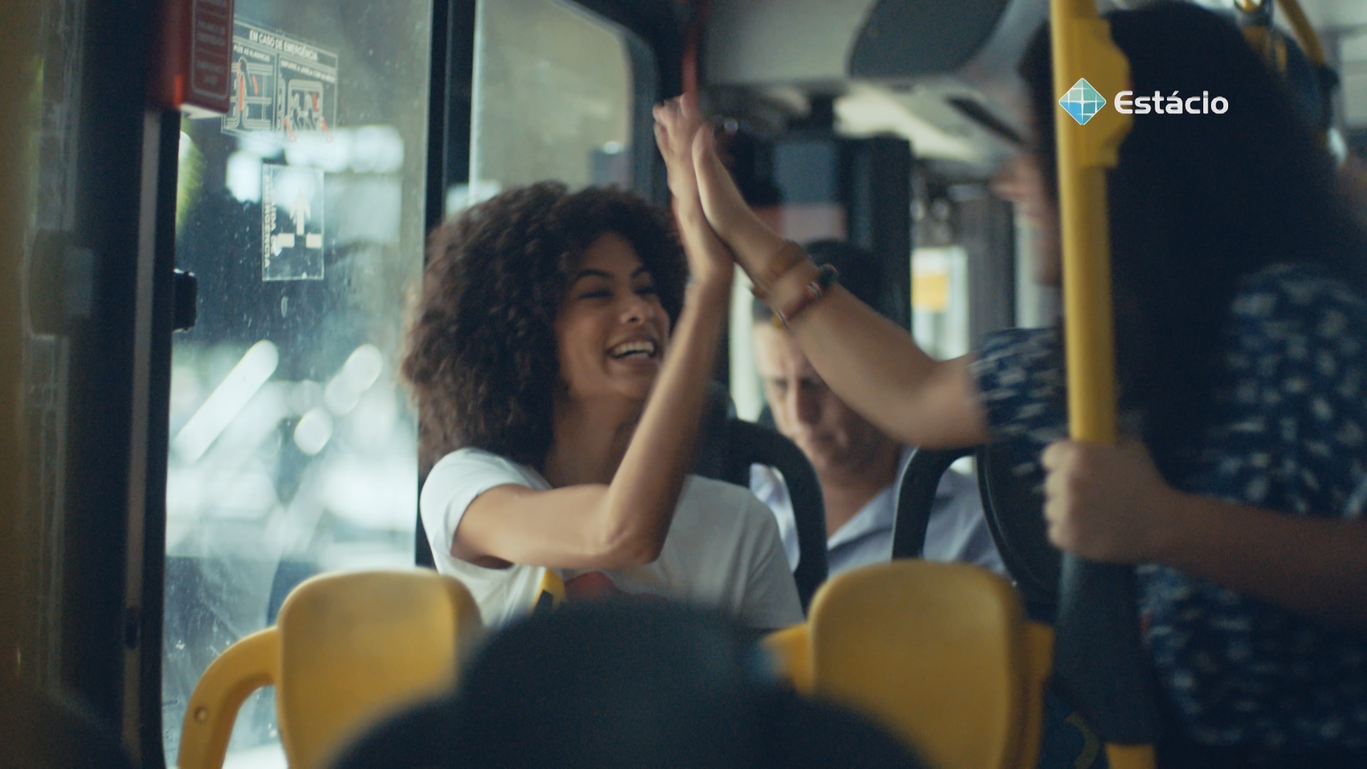 Dentro de um ônibus, duas estudantes se cumprimentam.