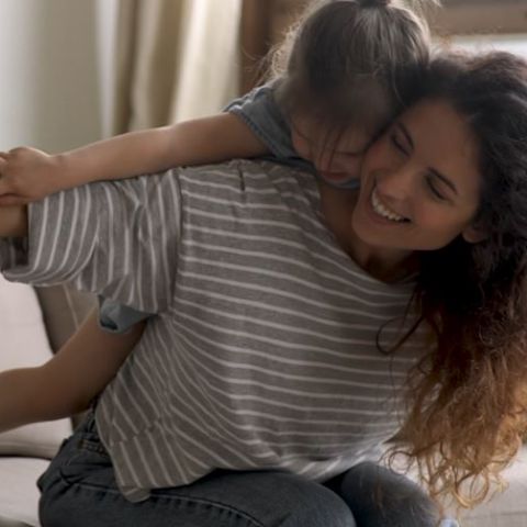 Mãe e filha brincam juntas sorrindo, fazendo o formato de asas com os braços