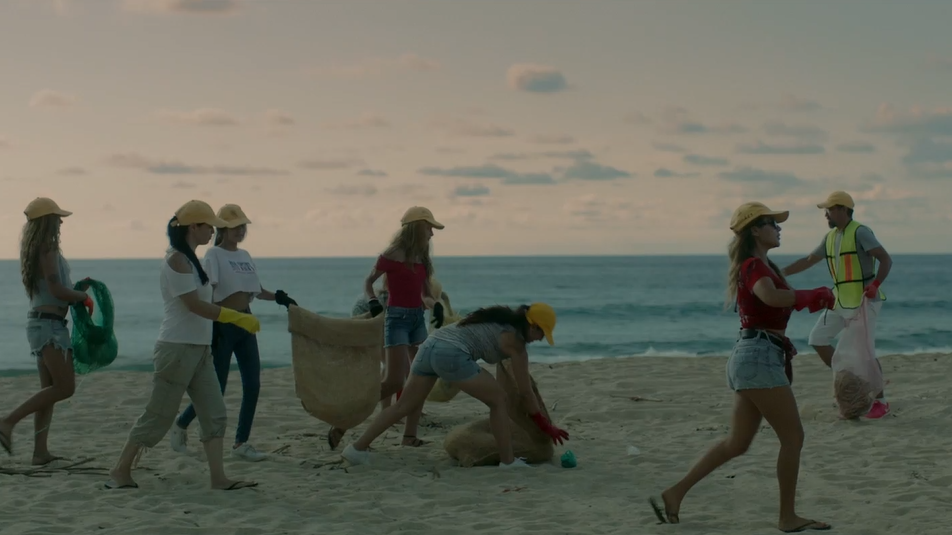 Grupo de pessoas andando na areia da praia, recolhendo lixo