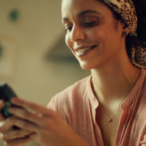 Foto de uma mulher com leve sorriso enquanto usa o celular